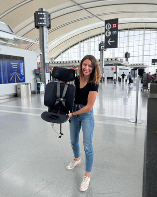  A mom holding a travel carseat at the airport.