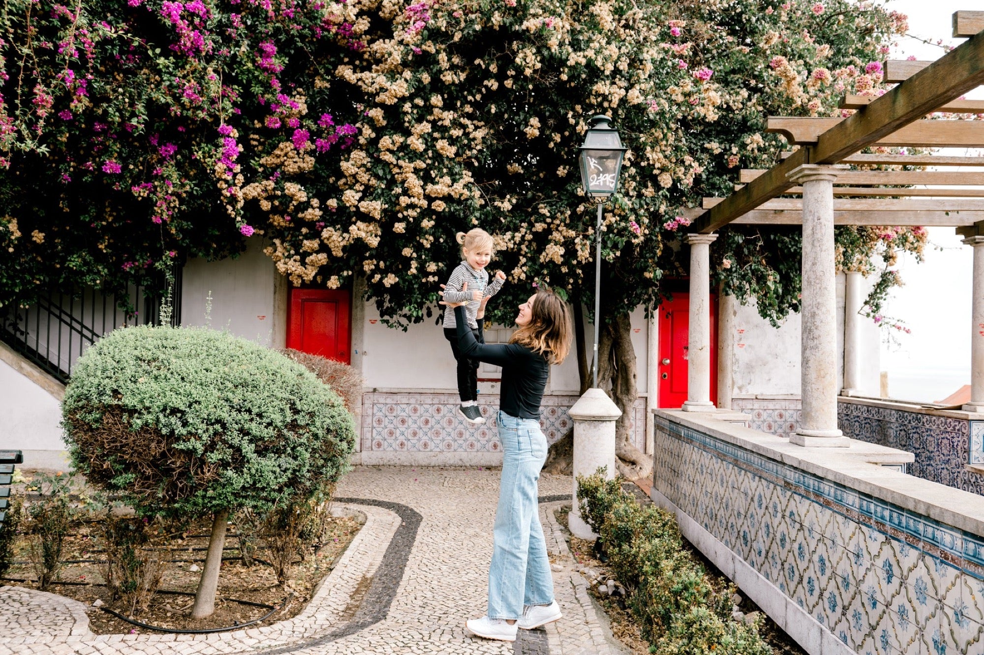 Olga lifting her daughter under bougainvillea on a tiled terrace in Lisbon